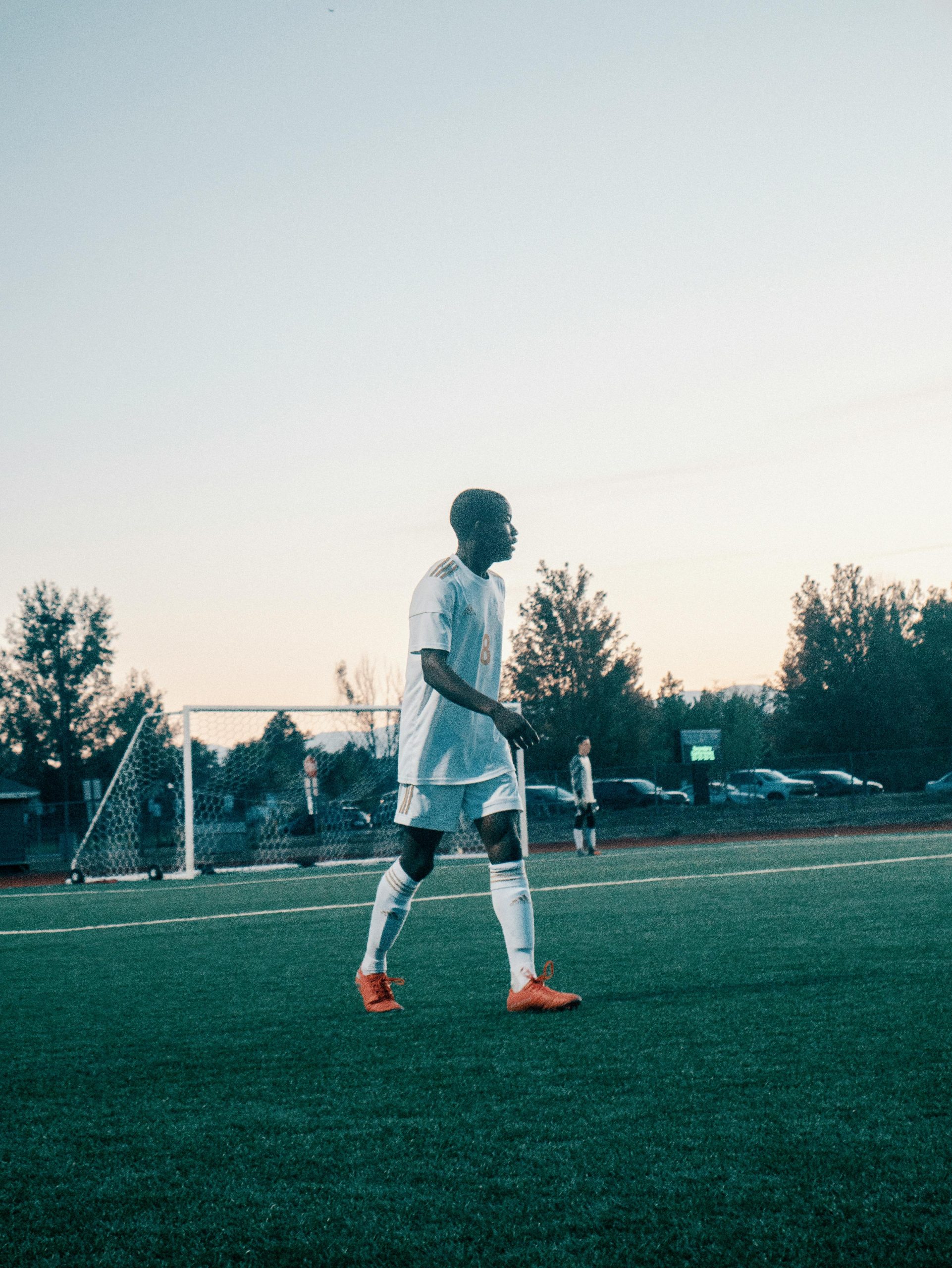 pexels-photo-3041176-3041176-1 Teen soccer player in action on the field during dusk. Outdoor sports activity with goal visible.
